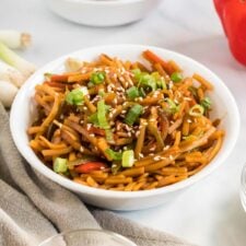 Bowl of vegan low mein noodles topped with green onion and sesame seeds.