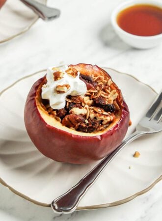 Baked apple stuffed with oats and nuts on a plate topped with a small dollop of whipped cream.