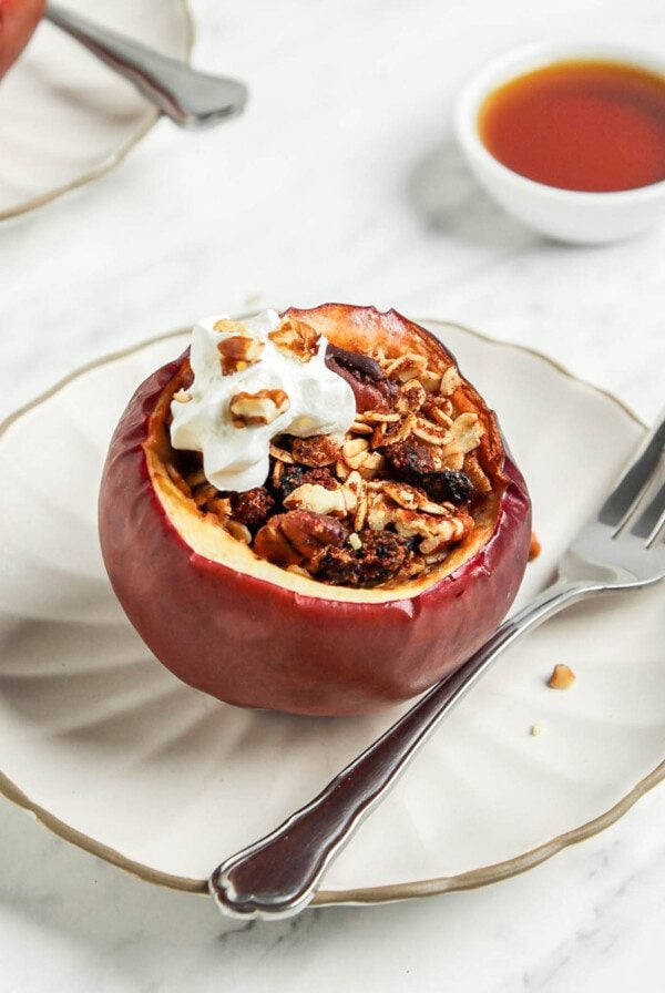 Baked apple stuffed with oats and nuts on a plate topped with a small dollop of whipped cream.