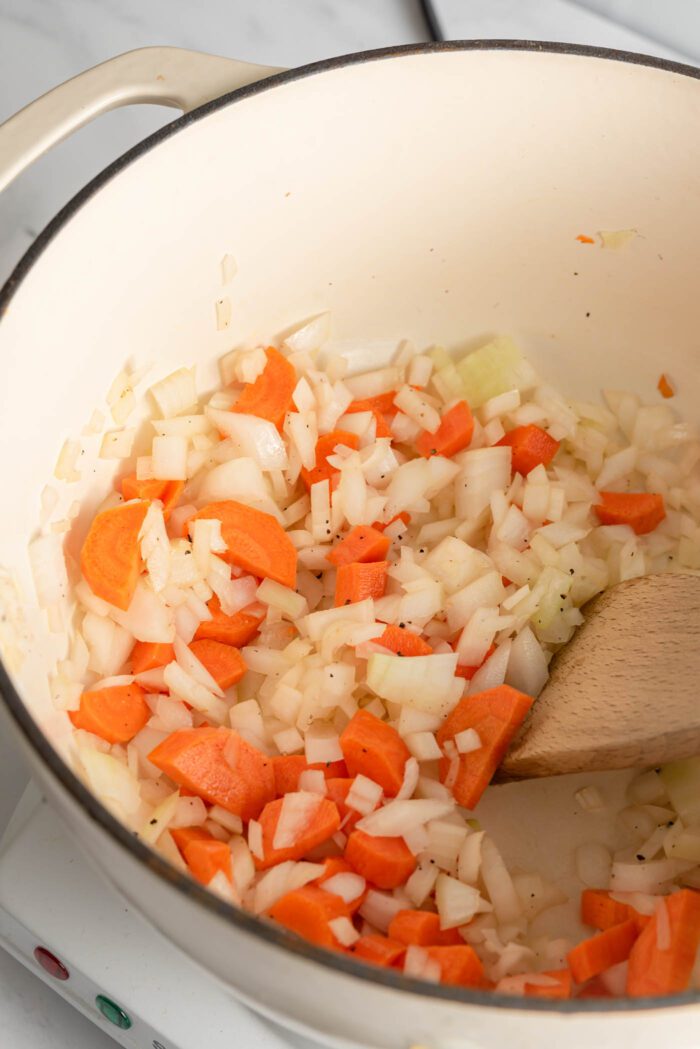 Sautéed onion, garlic and carrot in a large soup pot with a wooden spoon.