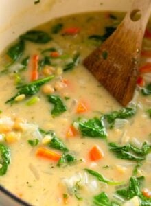 Large soup pot of lemon orzo soup with spinach and chickpeas. A wooden spoon rests in the pot.