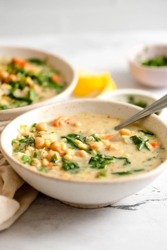 Two bowls of vegetarian Greek lemon orzo soup with chickpeas and spinach.