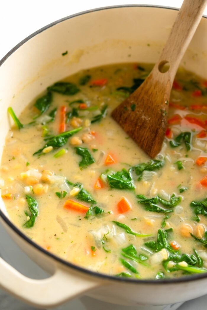 Large soup of lemon orzo soup with spinach and chickpeas. A wooden spoon rests in the pot.