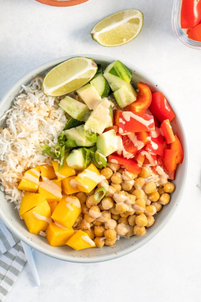 Overhead view into a bowl with chickpeas, mango, bell pepper, rice, cucumber and a drizzle of sauce.