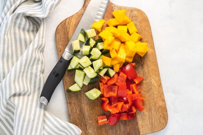 Chopped mango, cucumber and bell pepper on a cutting board.