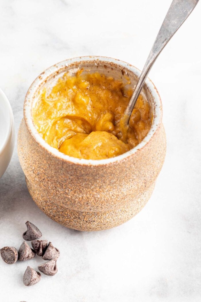 Mixed pumpkin batter in a mug with a spoon.