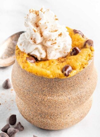 Close up of a pumpkin mug cake with chocolate chips and whipped cream.