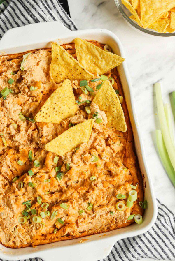 Overhead view of a dish of baked buffalo dip topped with scallions with some tortilla chips in the dip.