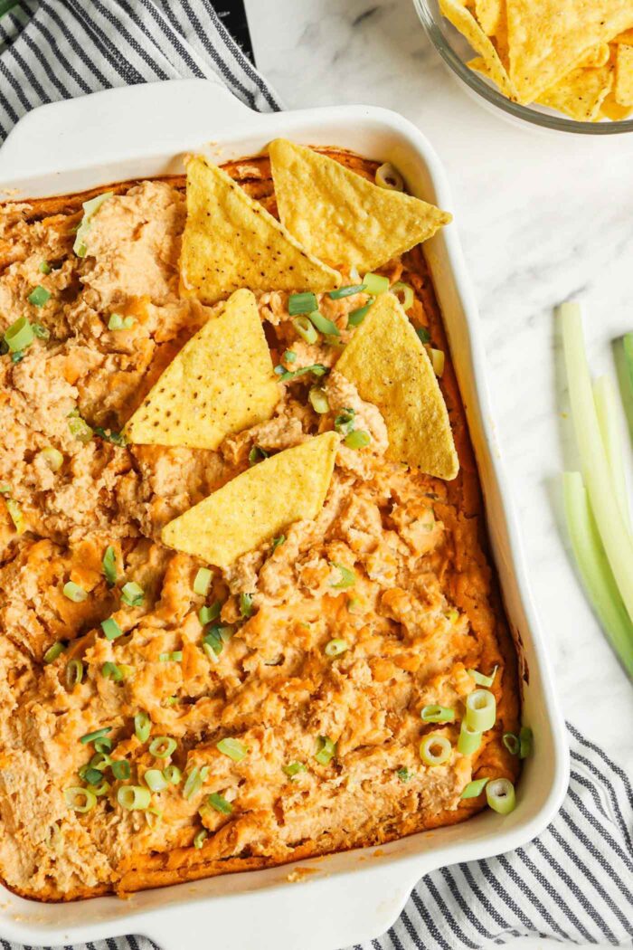 Overhead view of a dish of baked buffalo dip topped with scallions with some tortilla chips in the dip.