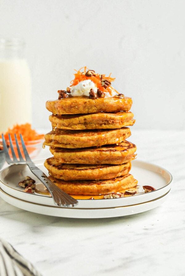 Stack of 6 thick carrot pancakes on a small plate. Fork rests on the plate.