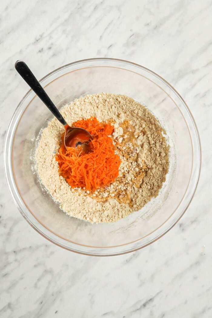 Dry pancake batter ingredients in a mixing bowl with grated carrot and water.