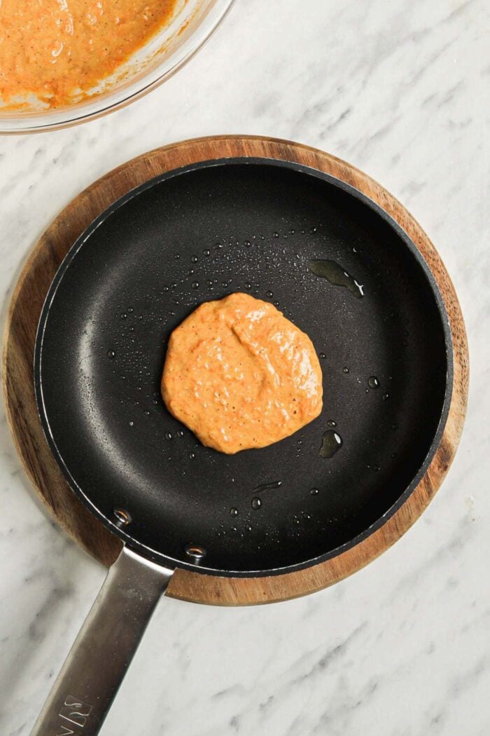 One small carrot pancake cooking in a hot skillet.