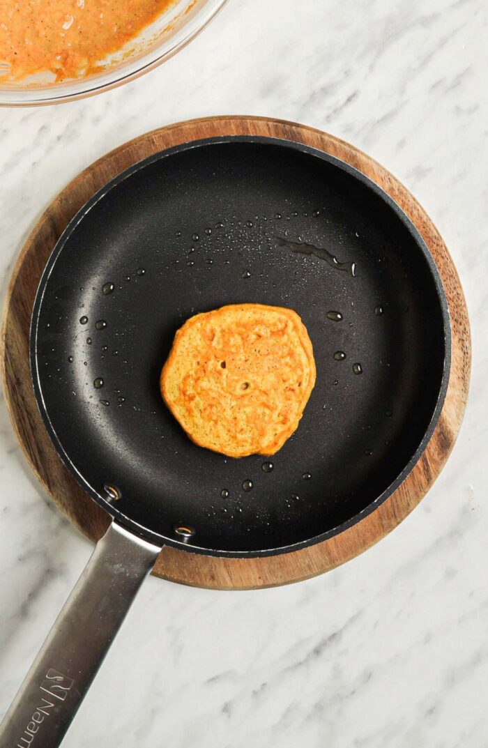 One small cooked carrot pancake cooking in a hot skillet.
