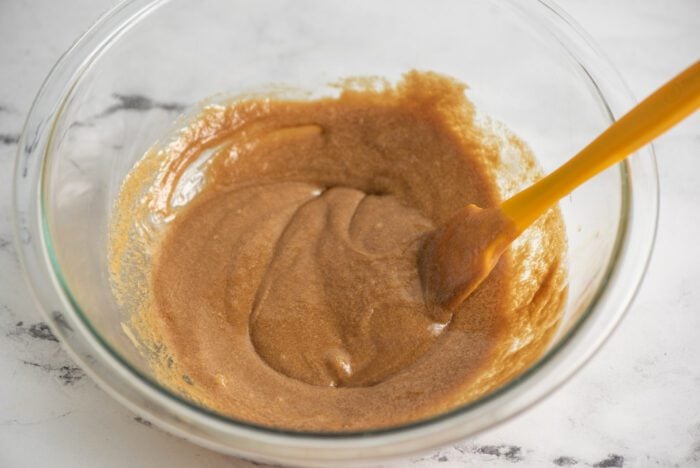 Maple syrup and tahini mixed together in a glass mixing bowl with a small spatula.