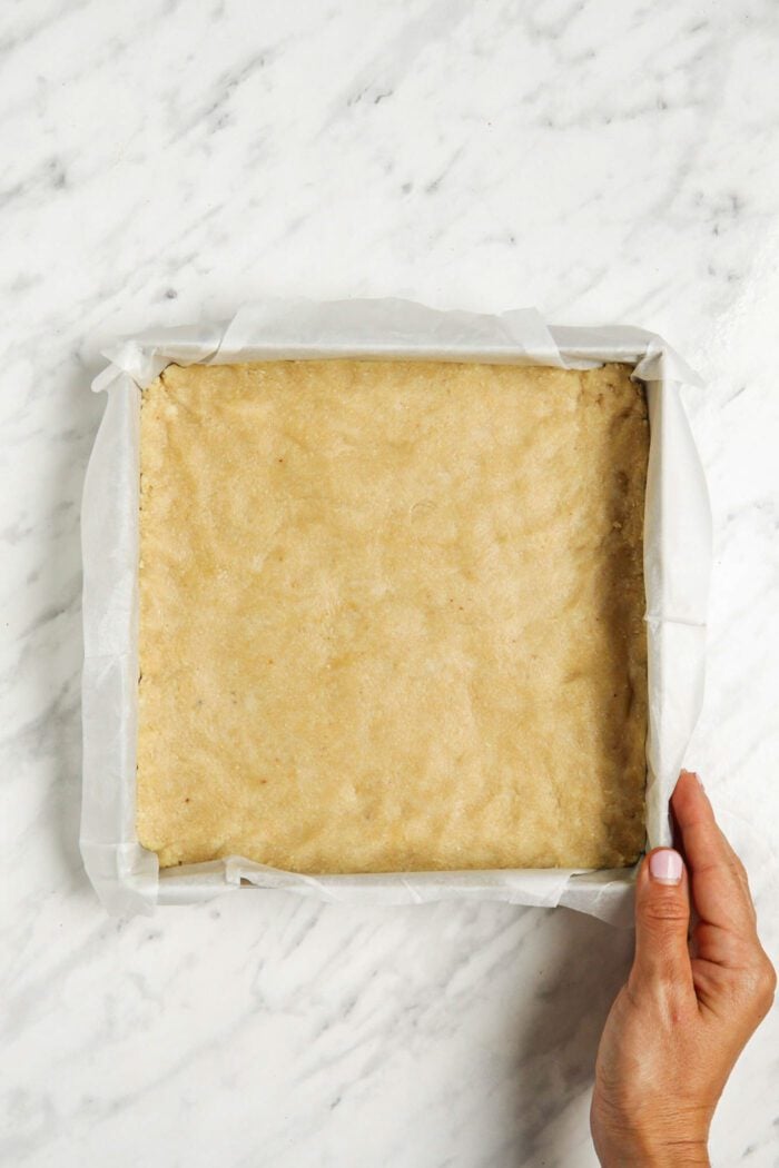 Shortbread dough pressed into a square baking pan. A hand is holding one corner of the pan.