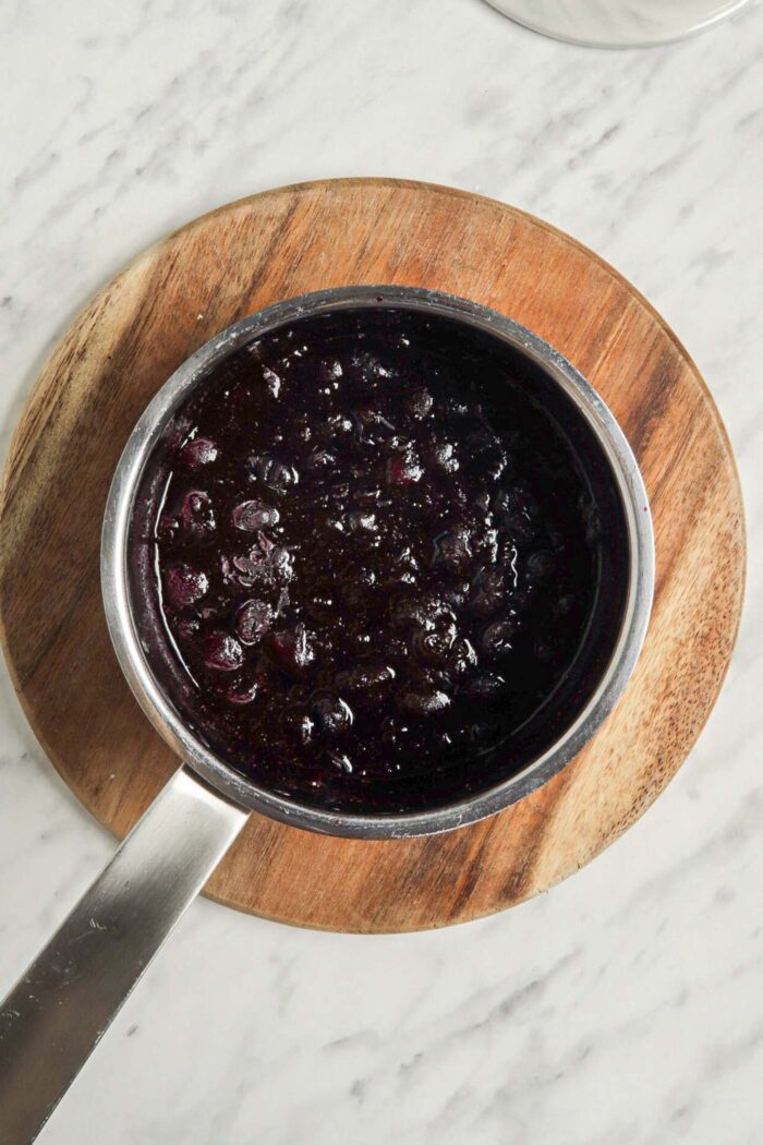 Mashed frozen blueberries in a small saucepan sitting on a cutting board.