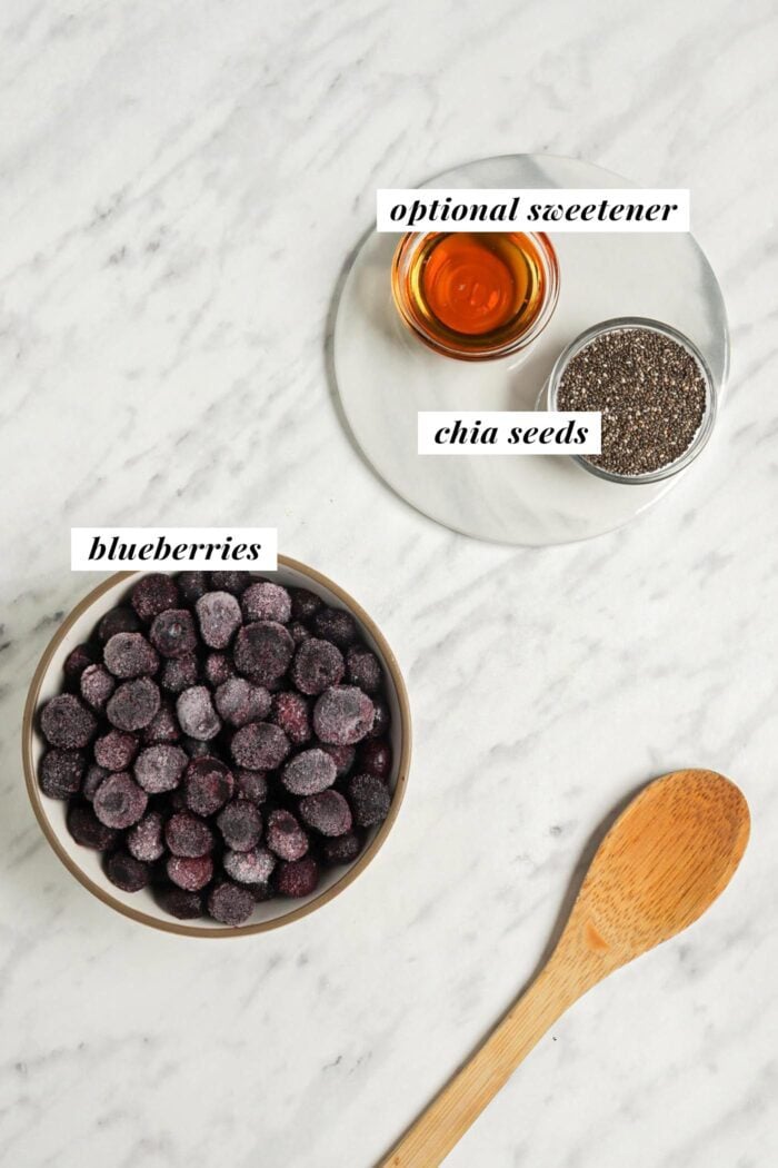 Blueberries, chia seeds and maple syrup each in a small bowl on a marble surface.