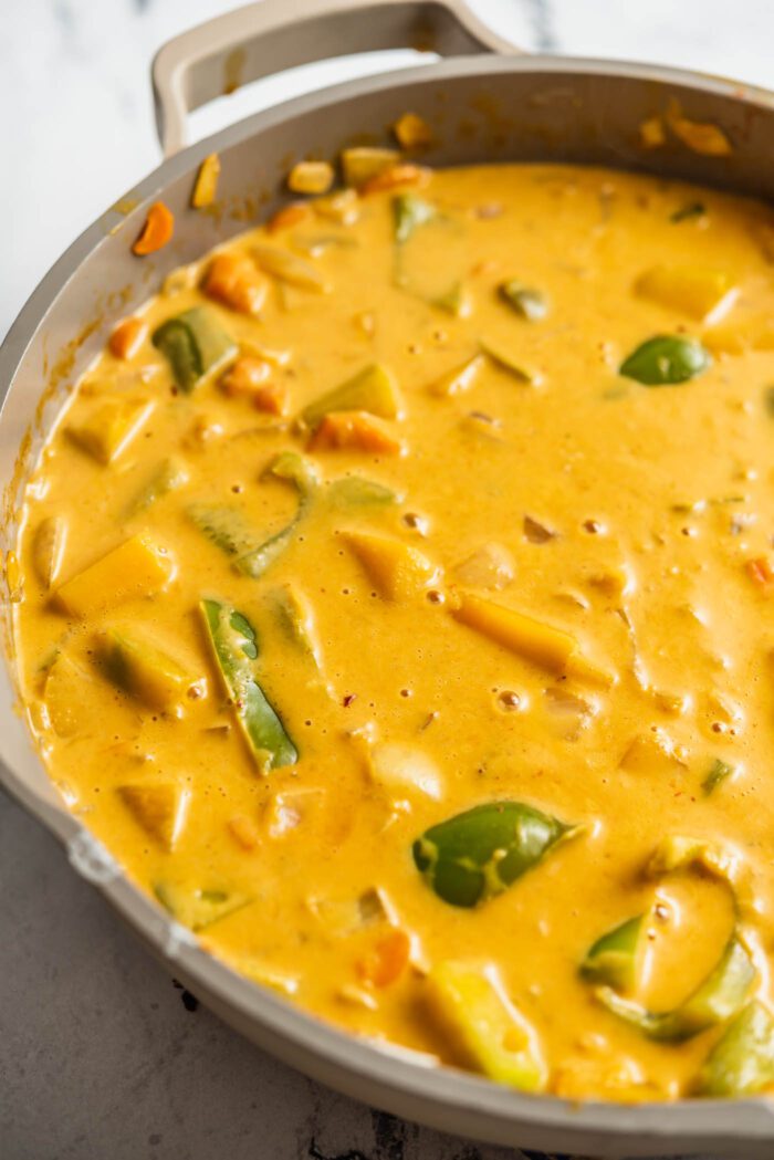 Creamy red curry with veggies cooking in a skillet.