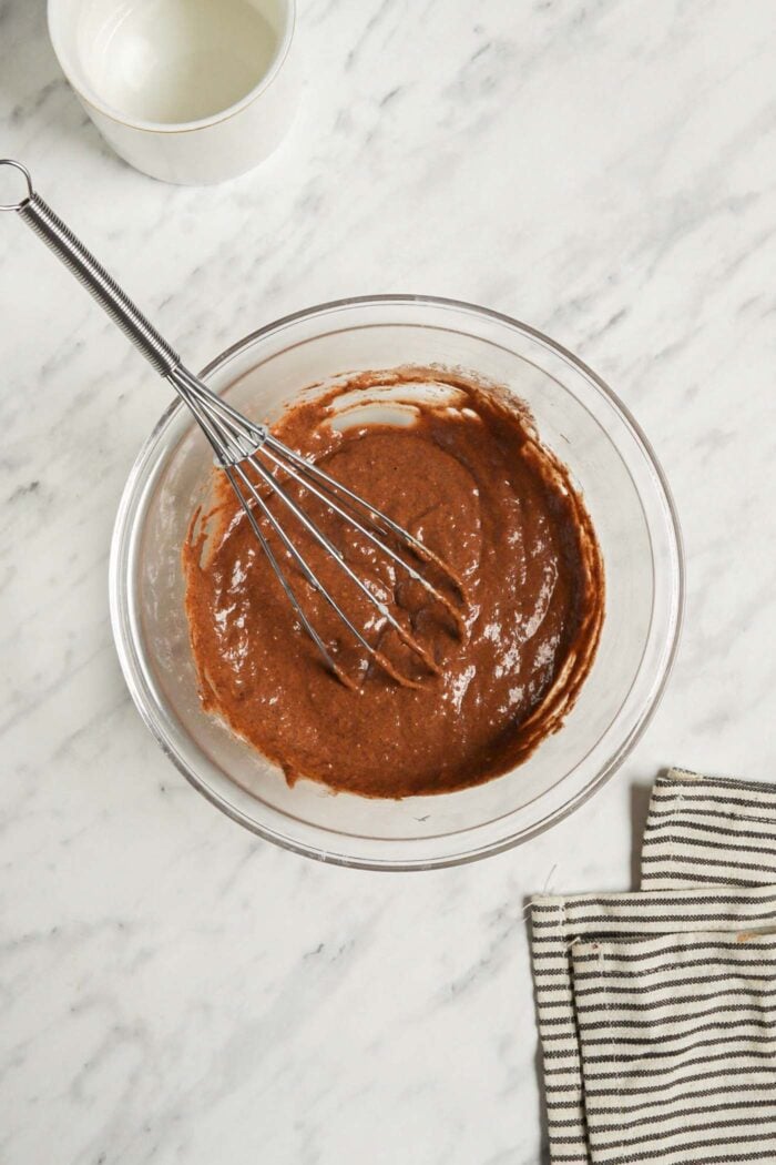 Chocolate cake batter mixed together in a glass mixing bowl with a whisk.