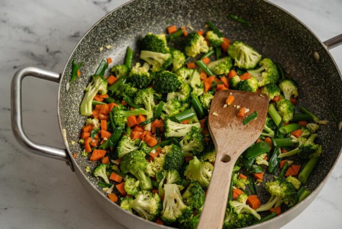 Broccoli, carrot, garlic and green onion cooking in a skillet.