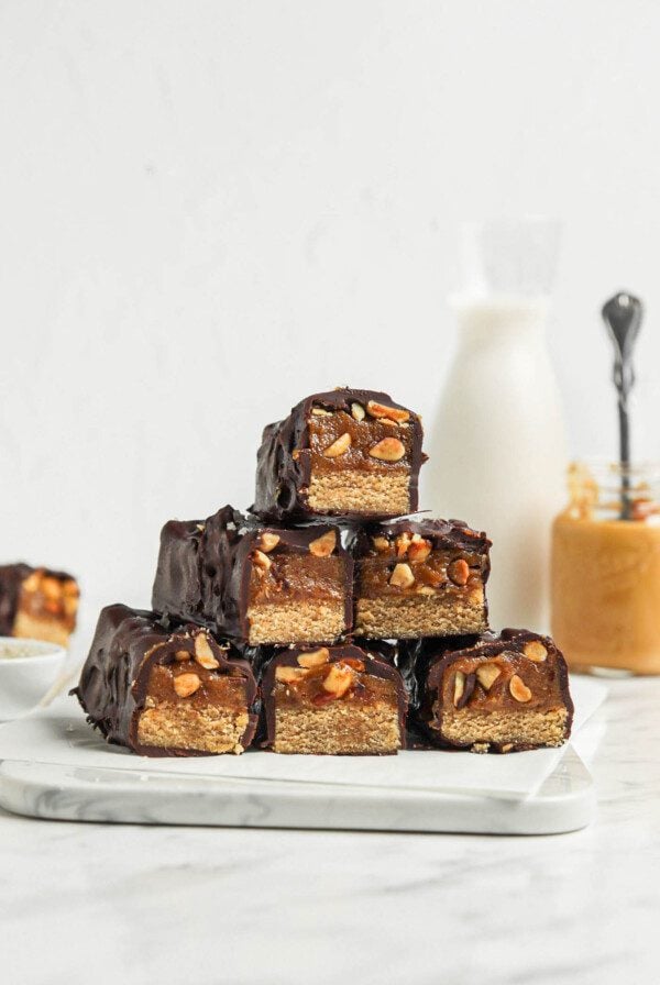 Stack of homemade Snickers bars with a cookie base, caramel layer and chocolate coating.