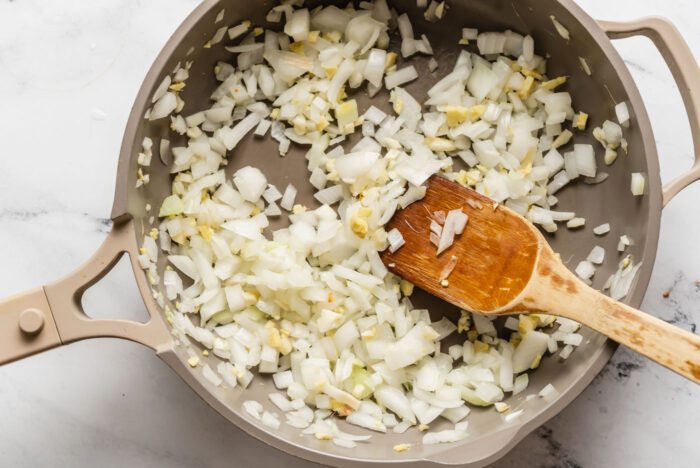 Onion, garlic and ginger cooking in a pan on the stovetop with a wooden spoon.