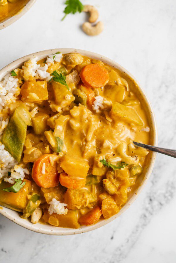 Bowl of red squash curry with bell peppers and carrots served over rice and topped with a few pieces of fresh cilantro.