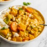 Bowl of squash and vegetable red curry over rice in a bowl. A spoon rests in the bowl.