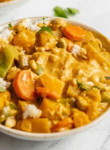 Bowl of squash and vegetable red curry over rice in a bowl. A spoon rests in the bowl.