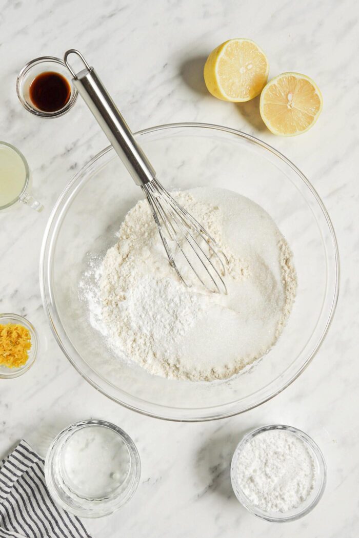 Dry baking ingredients being mixed together in a glass mixing bowl with a whisk.