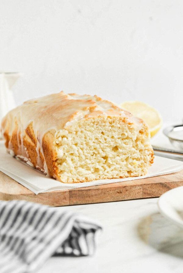 Sliced lemon pound cake topped with glaze on a cutting board lined with parchment paper.