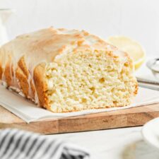 Sliced lemon pound cake topped with glaze on a cutting board lined with parchment paper.