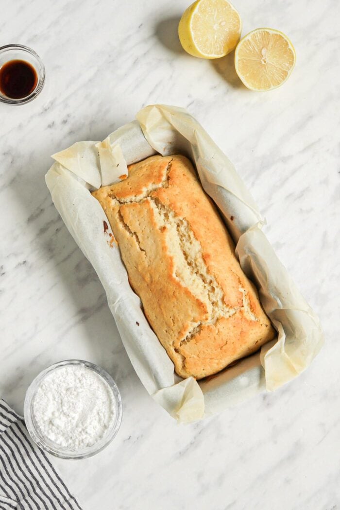 Baked lemon bread in a loaf pan lined with parchment paper.