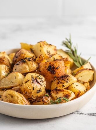 Close up of a bowl of rosemary lemon roasted potatoes with a sprig of rosemary in the bow.