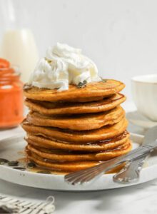 Stack pumpkin pancakes topped with whipped cream and maple syrup.