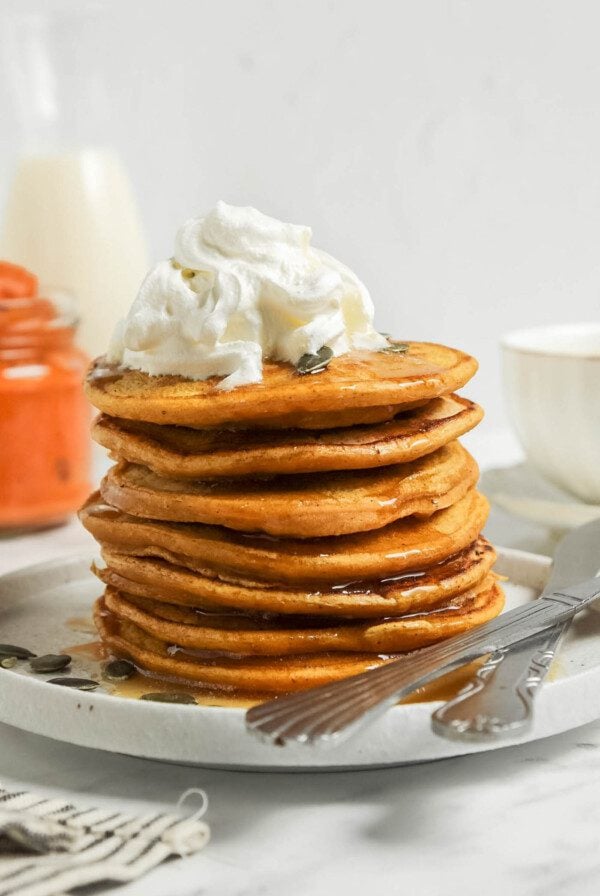 Stack pumpkin pancakes topped with whipped cream and maple syrup.