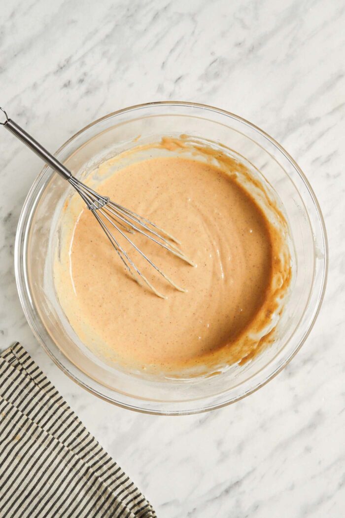 Thick pumpkin pancake batter in a mixing bowl with a whisk resting in the bowl.