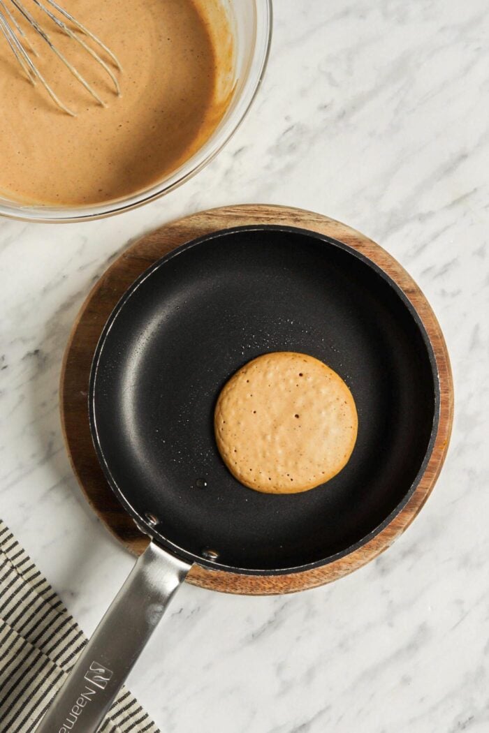 One pumpkin pancake cooking in a hot skillet.