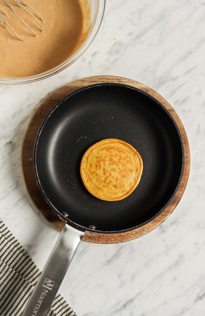 One pumpkin pancake cooking in a non-stick skillet.