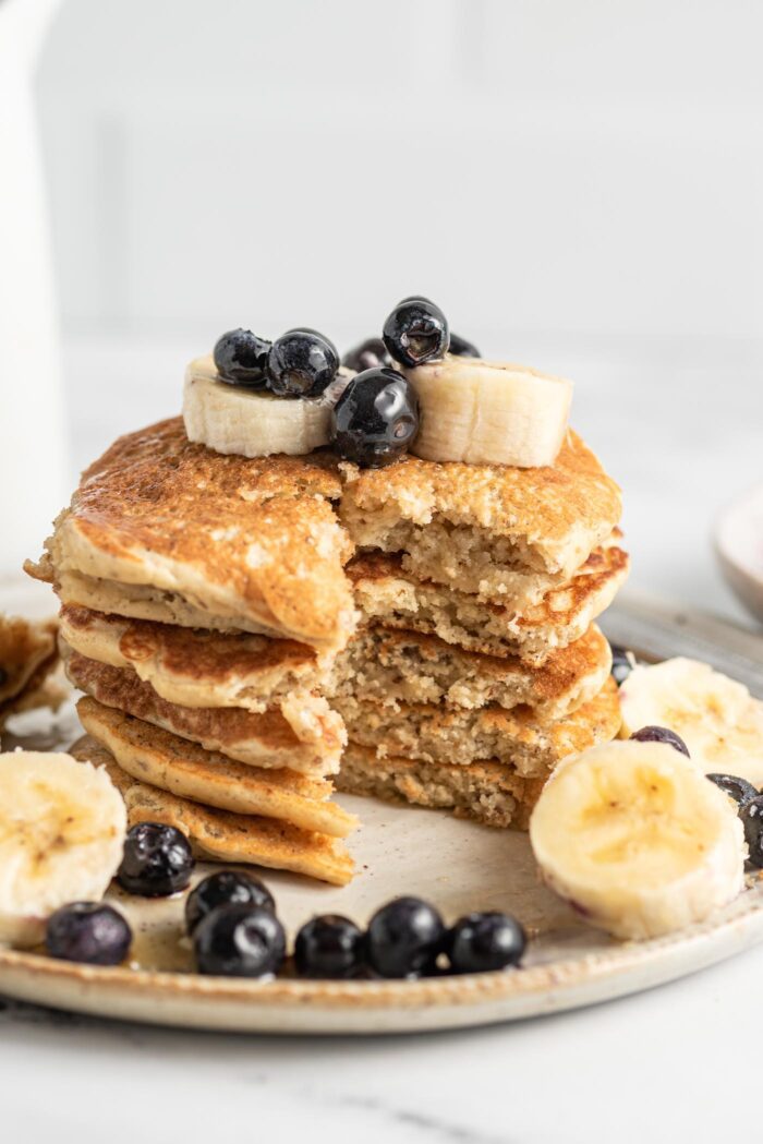 Close up of a stack of pancakes that have been sliced to show the texture inside. The pancakes are topped with blueberries and banana.