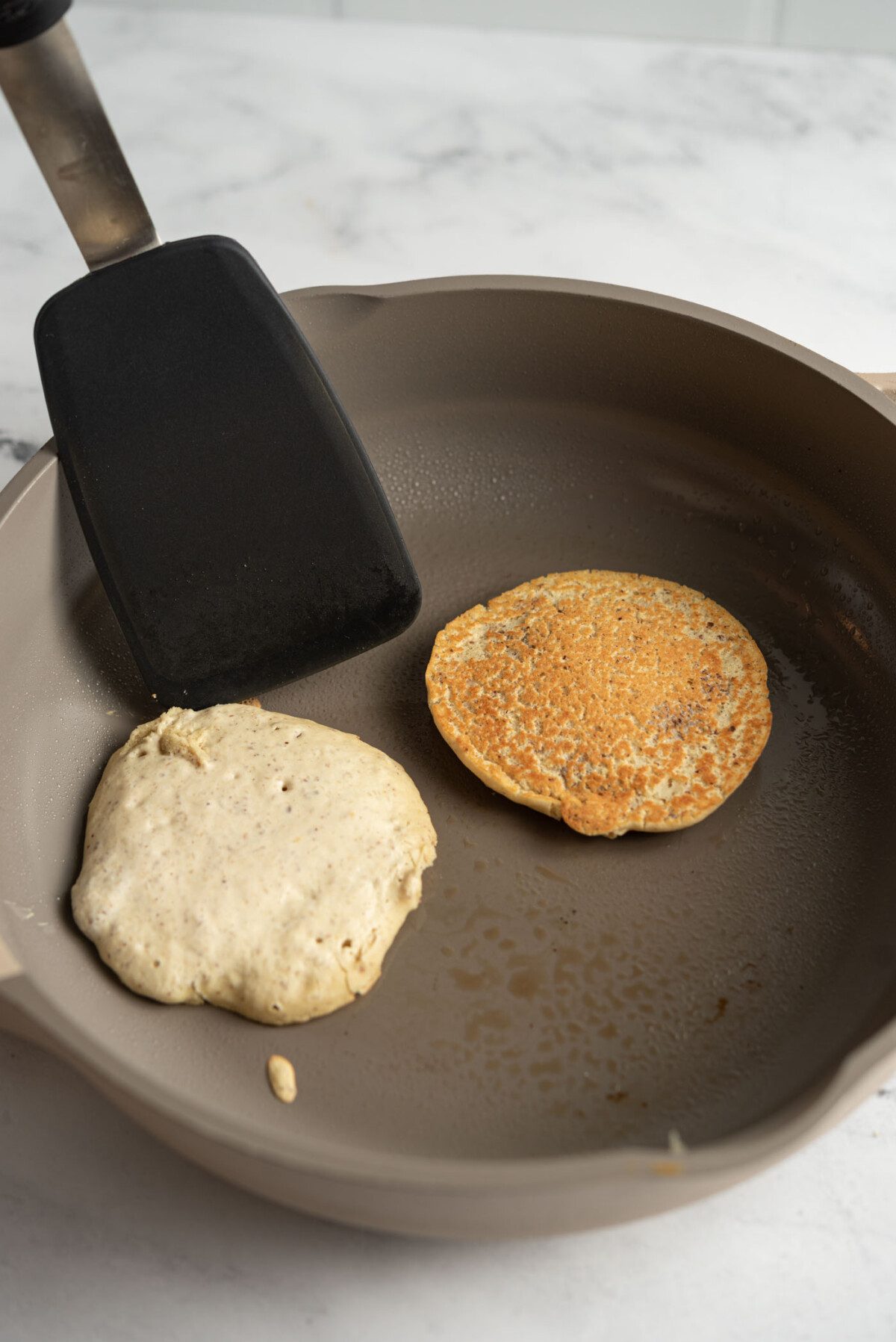 Spatula flipping a pancake in a hot skillet.