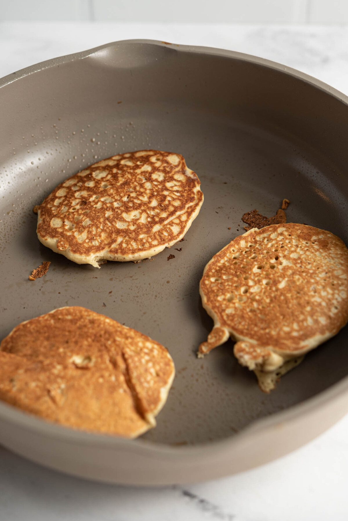 3 quinoa flour pancakes cooking in a skillet.