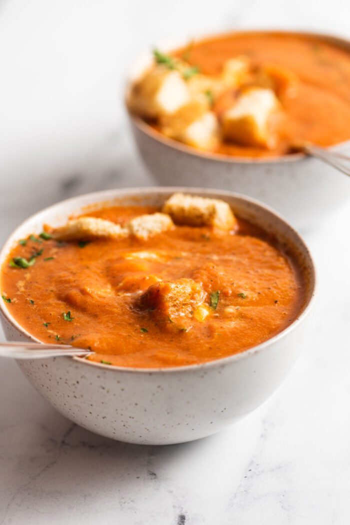 Bowl of roasted red pepper tomato soup topped with toasted bread, cream and basil.
