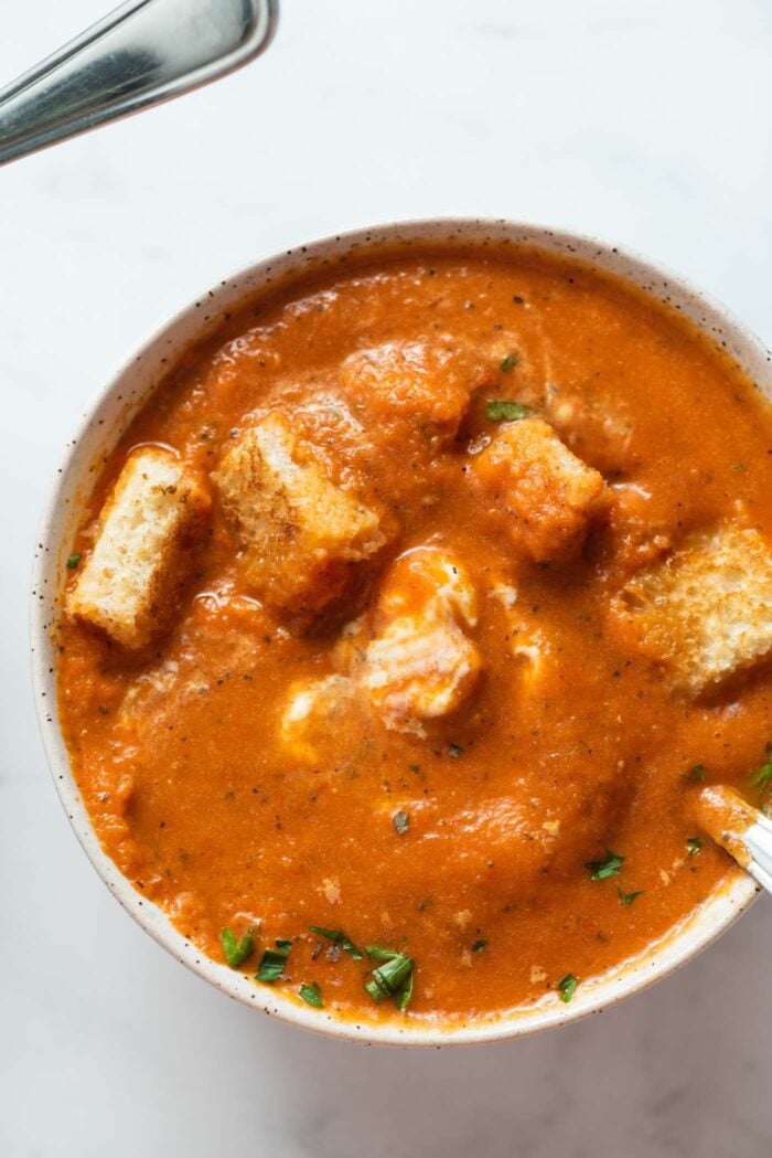 Overhead view of a bowl of red pepper tomato soup topped with cubes of toasted bread.