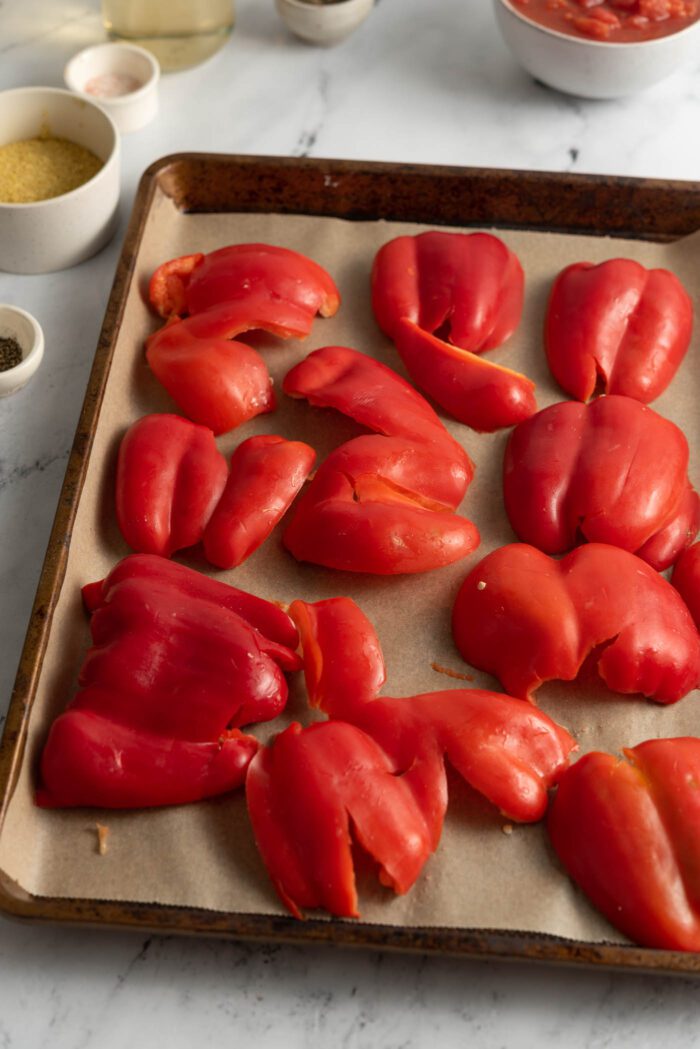 Bell peppers smashed down on a baking tray in preparation of making roasted red peppers.