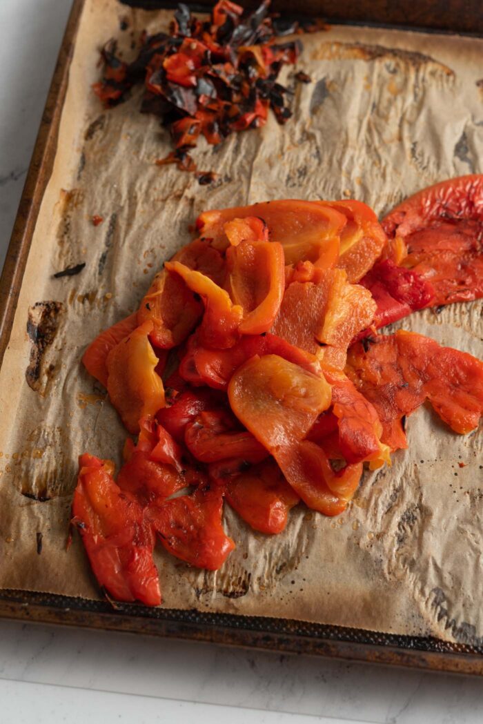 Peeled roasted red peppers in a pile on a baking tray.