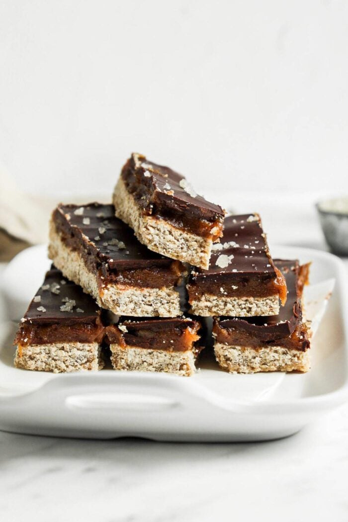 Stack of 6 homemade Twix-style bars with a shortbread, caramel and chocolate layer on a small dish.
