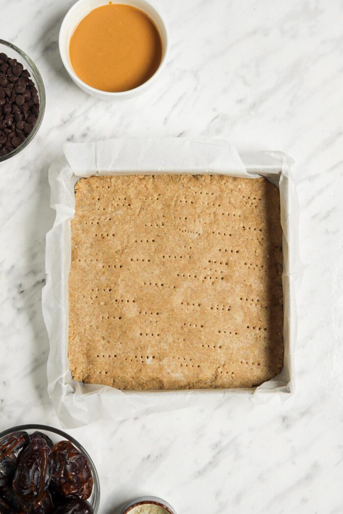 Baked shortbread crust in a baking pan lined with parchment paper.
