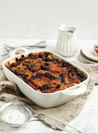 Baked bread pudding in a baking dish. A mesh strainer rests beside dish.