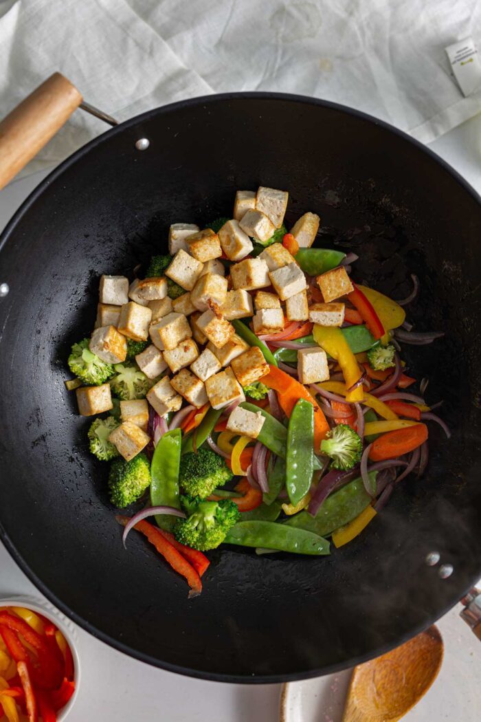 Sliced vegetables and cubed tofu cooking in a large wok.